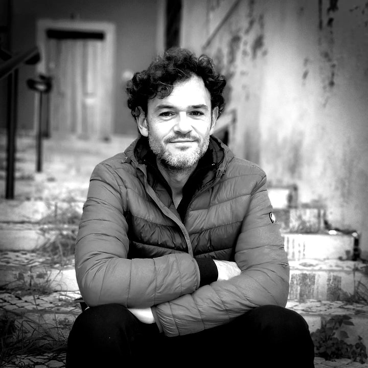 Black and white photo of Lejandrier sitting on an outdoor staircase, looking at the camera and smiling slightly