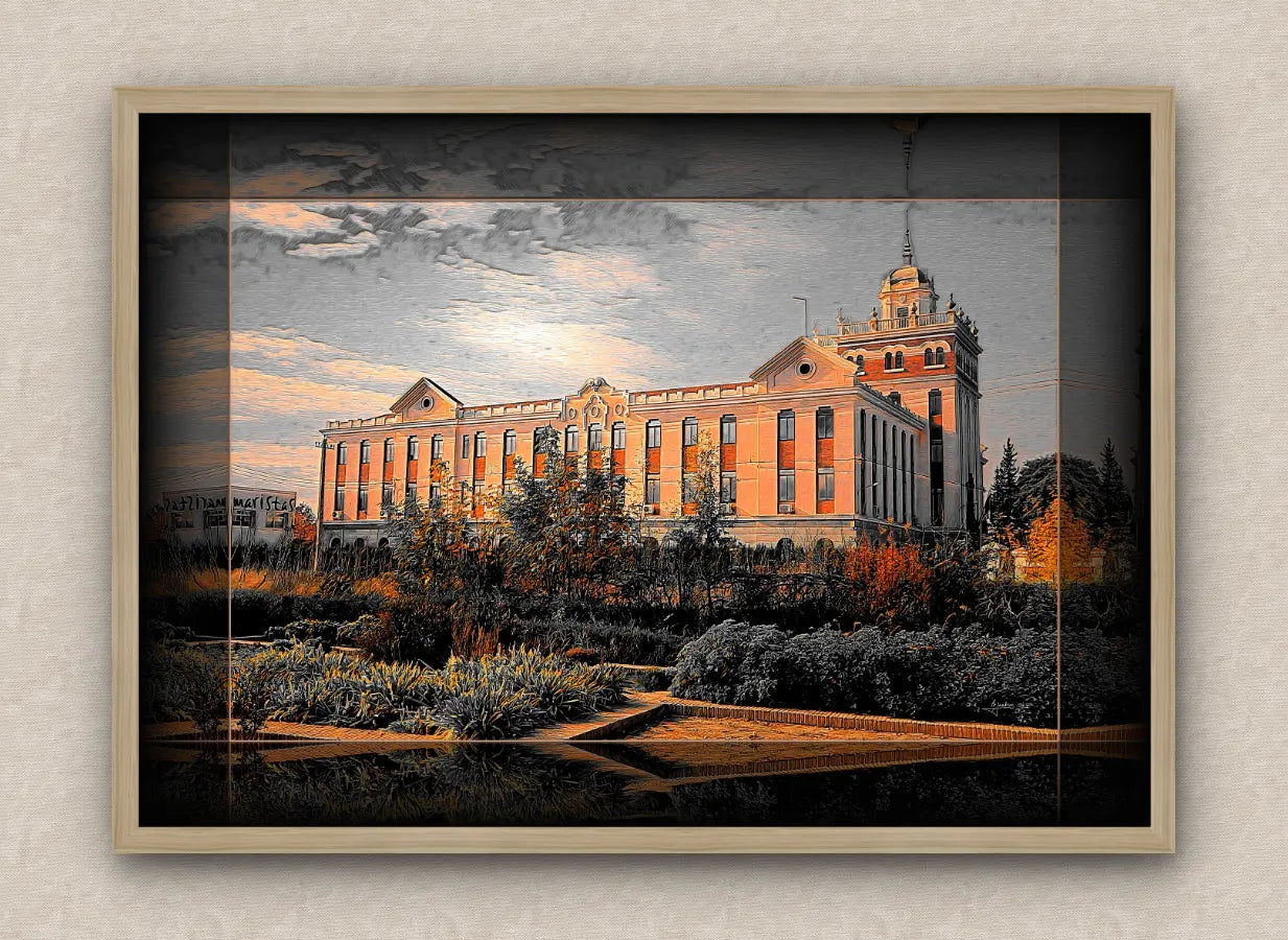 Landscape artwork with dark border and oak frame, showcasing a large building during sunset, surrounded by trees and bushes.