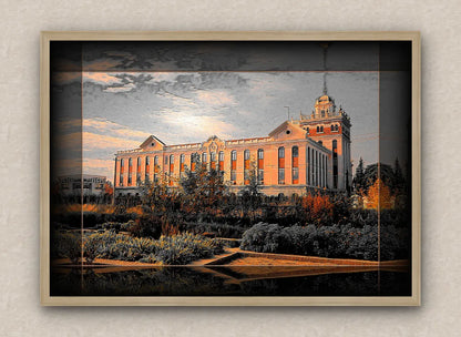 Landscape artwork with dark border and oak frame, showcasing a large building during sunset, surrounded by trees and bushes.