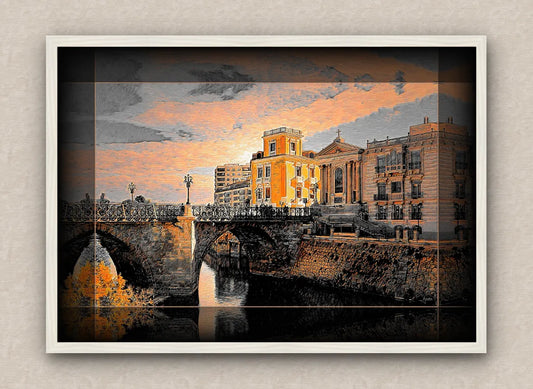 White framed artwork with dark border of a cityscape with an old bridge and buildings over a river during sunrise.