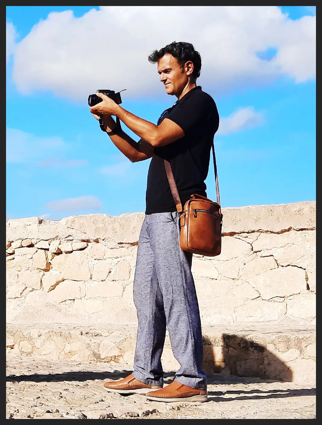 Man taking a photo with a camera against a stone wall and blue sky background
